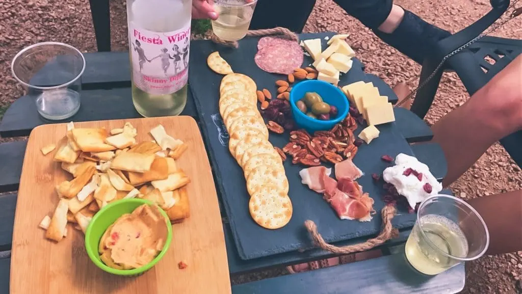 A table full of wine glasses, a board with hummus and pita chips, and a cheese and charcuterie board. 