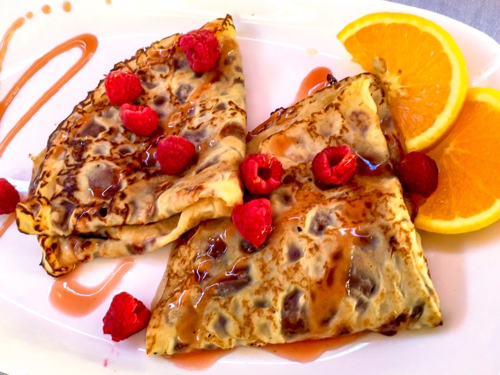Two crepes shaped in triangles with fresh raspberries and orange slices from CITY Restaurant in Kotor. 