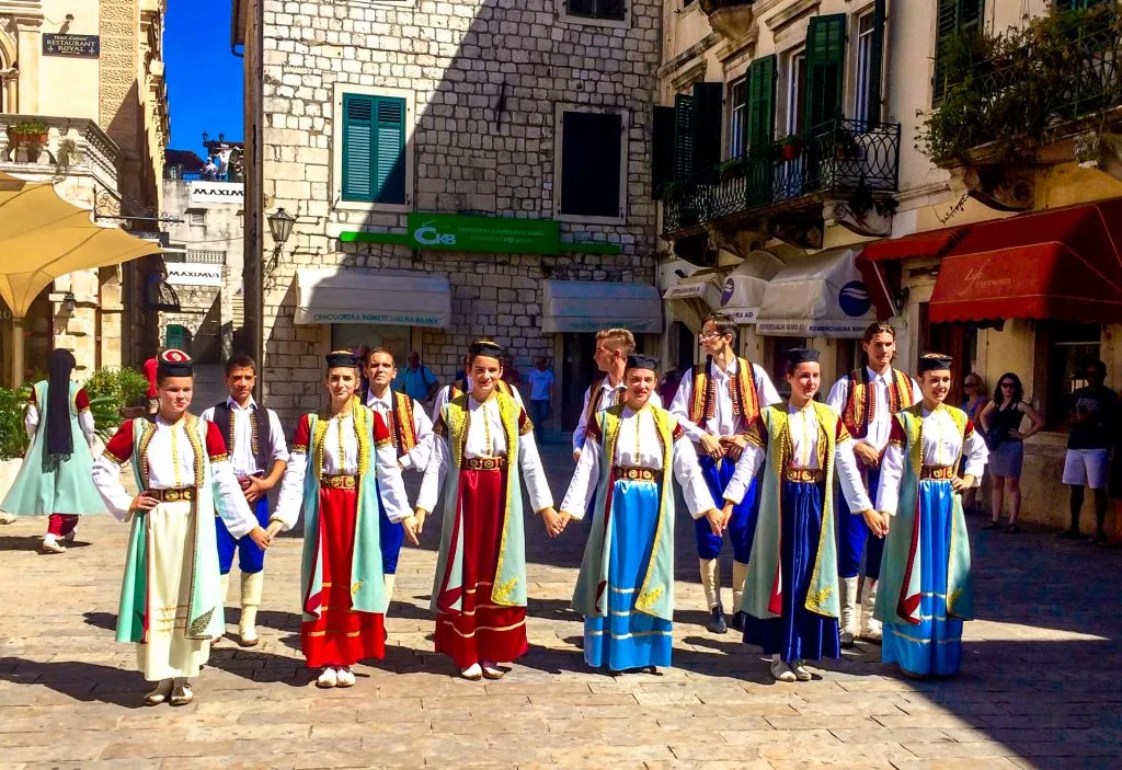 Several locals in Kotor dressed in bright red, blue and green dresses doing their traditional dance in the plaza of Old Town Kotor. 