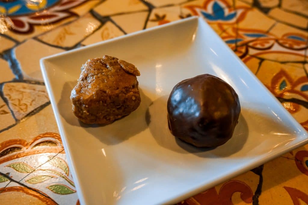 Two peanut butter dessert balls on a white square plate. The one on the right is covered in dark chocolate while the left one is not. 