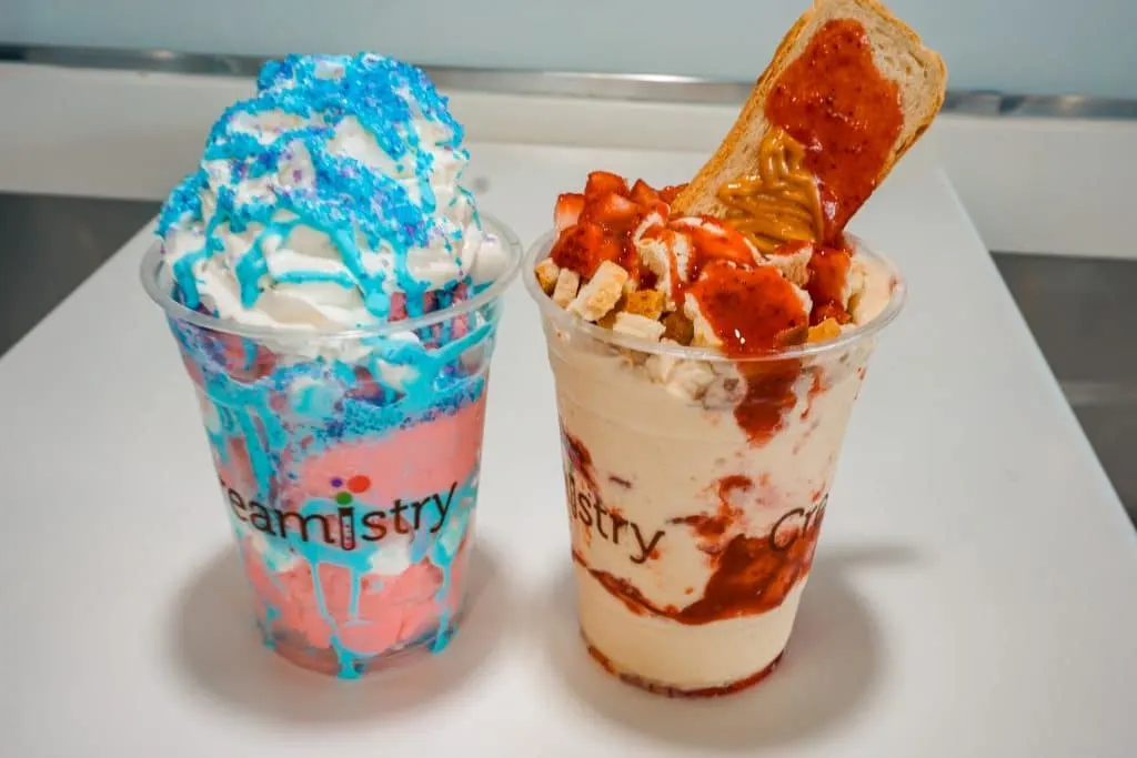Two liquid nitrogen ice cream sundaes from Creamistry. The left is called Unicorn and is bright pink with light blue drizzle and whipped cream. The one on the right is Peanut Butter and Jelly with peanut butter ice cream and red jelly drizzled. 