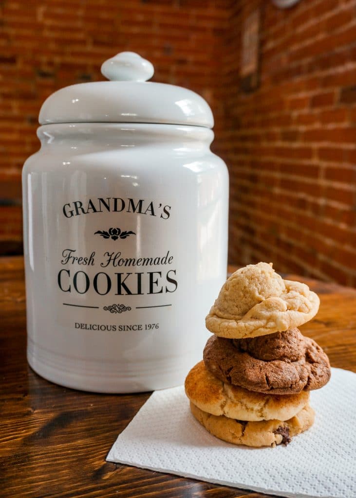 A white cookie jar labeled Grandma's Cookies with a stack of four cookies to the right of the jar.