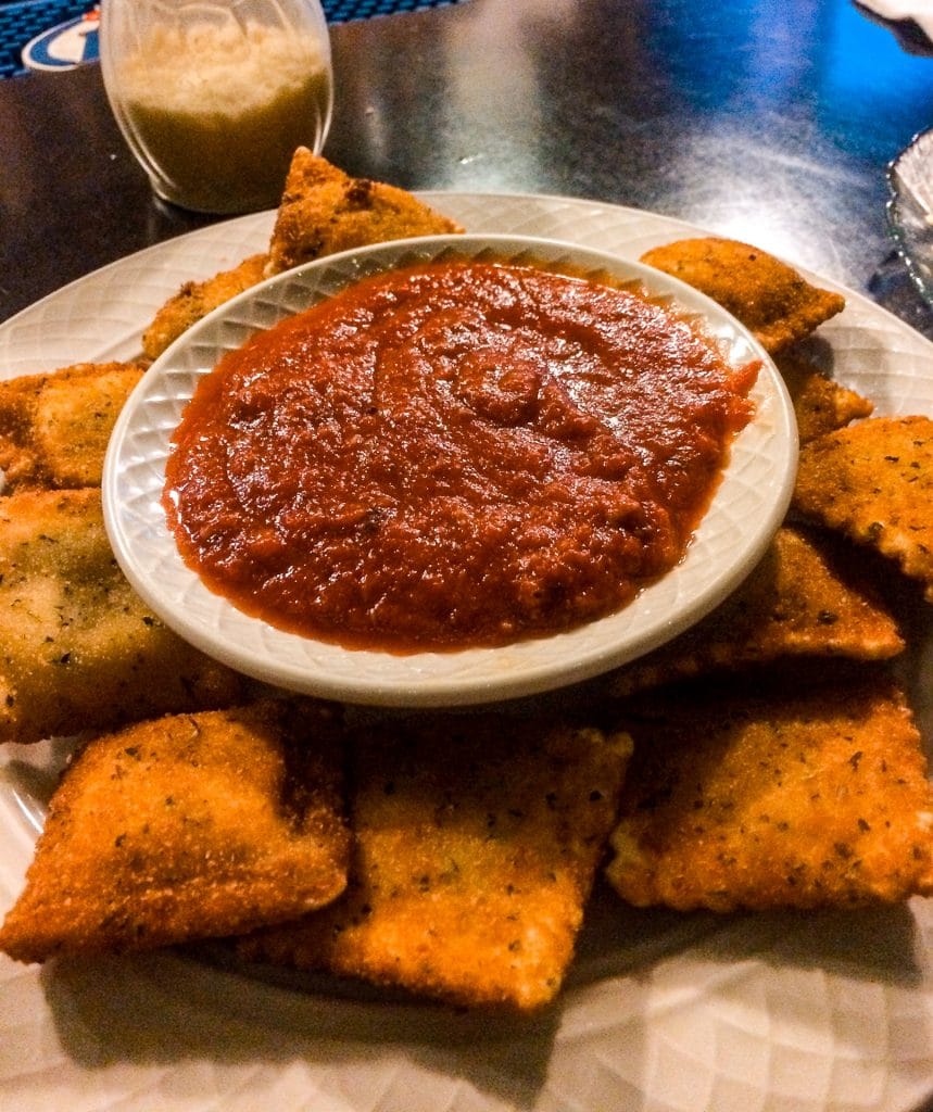 A platter filled with toasted ravioli and a small cup of marinara sauce in the middle from Pio's Restaurant. 