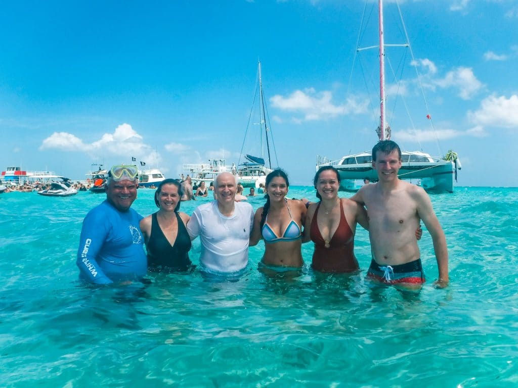 A family of five with a tour guide taking a photo in shallow water at Stingray City.