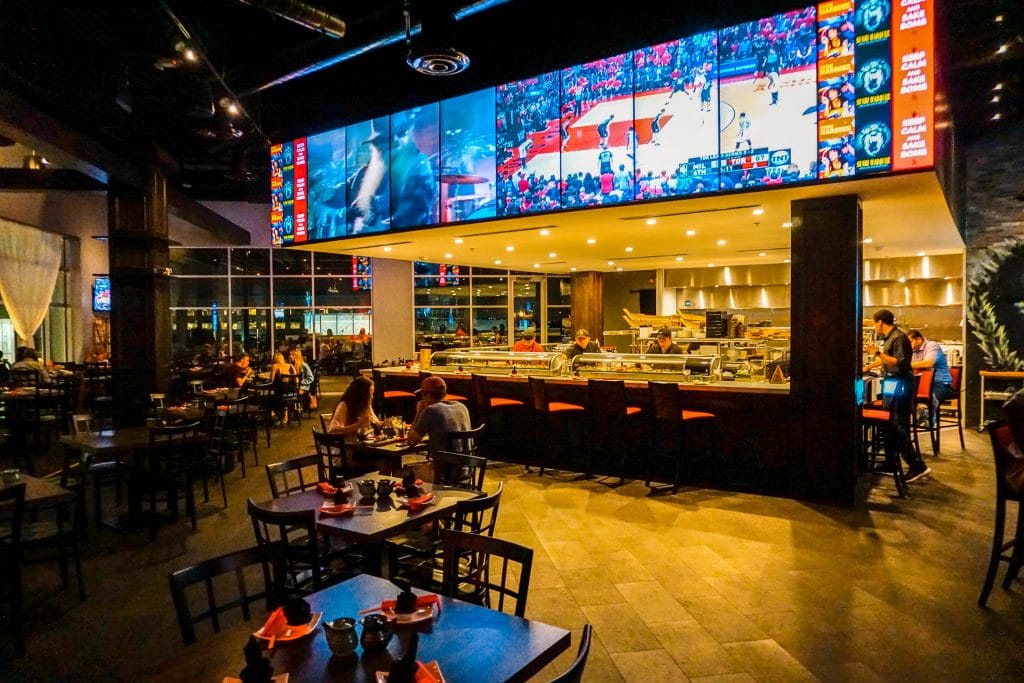 Inside the Sushi Marquee restaurant with TVs above the sushi bar. 