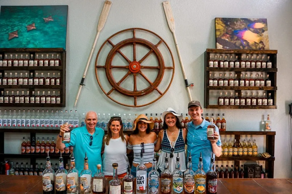 A group family photo of five at Cayman Spirits with bottles of alcohol in front of them. 