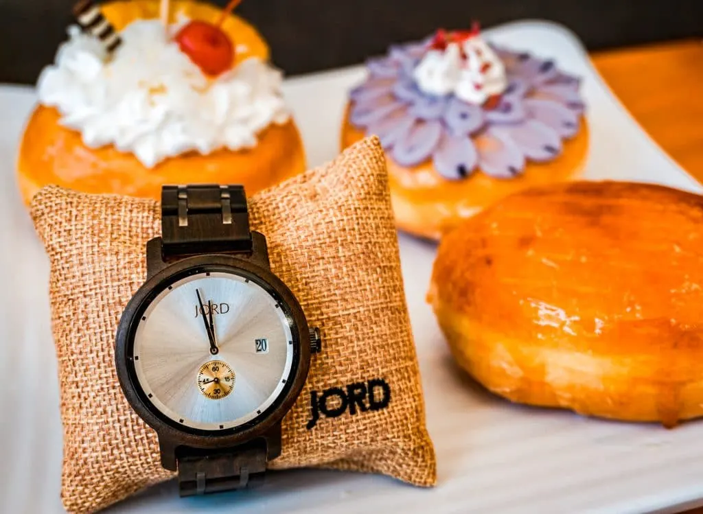 A minimalist wooden watch by JORD with three donuts in the background. 