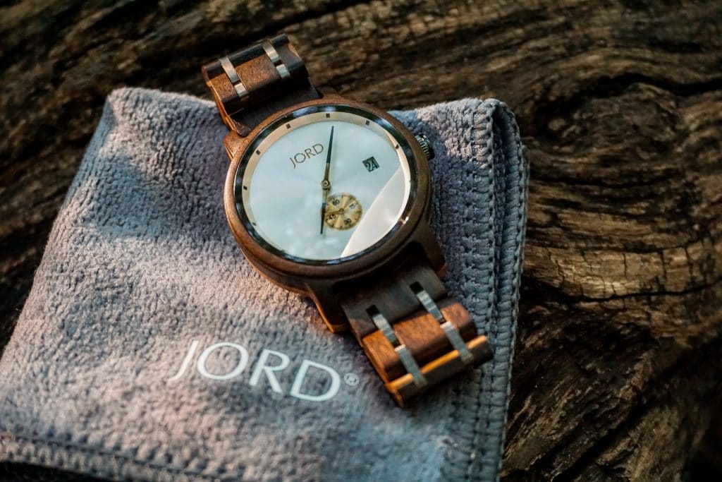 A JORD Hyde wooden watch laying at an angle on the corner of a gray square cloth resting on a wooden log.