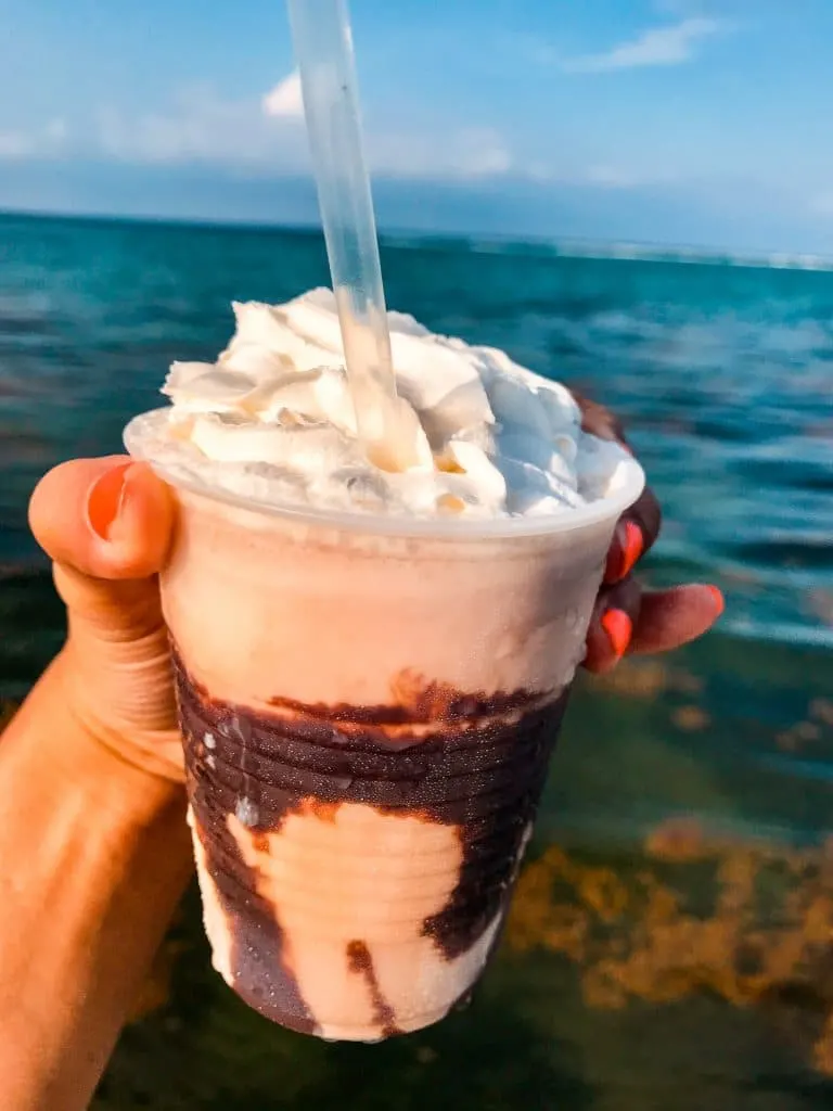 A Mudlside with the ocean in the background. There is chocolate drizzle down the cup and a dollop of whipped cream. 