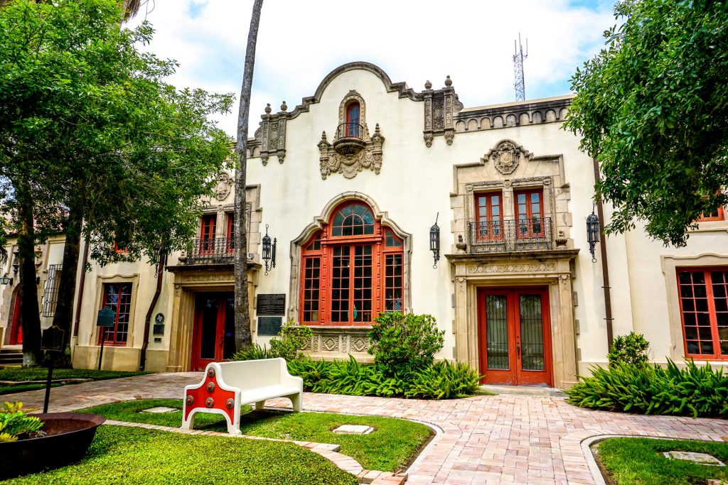A beautiful historical building in Brownsville, Texas with a red door and window panes.