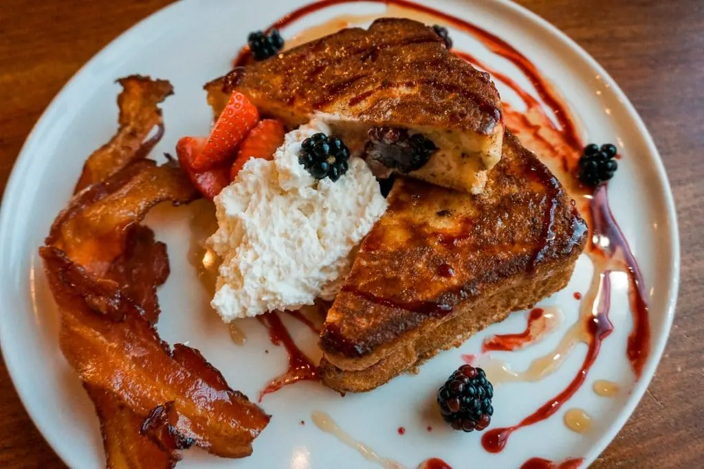 Stuffed Texas French toastier with a dollop of whipped cream , strips of bacon and berries.