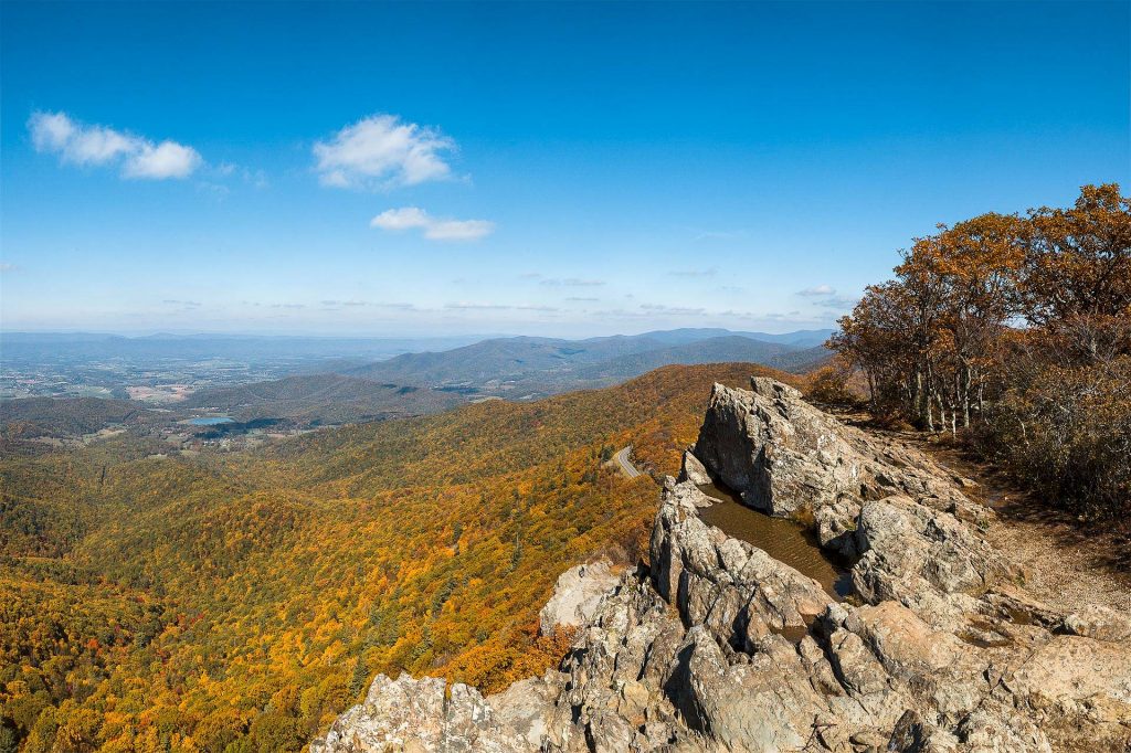 One of the best things to do in Washington D.C. in the fall is to go hiking and see the fall foliage. as shown in this picture a dramatic landscape of a mountain range covered in vibrant orange and yellow trees.
