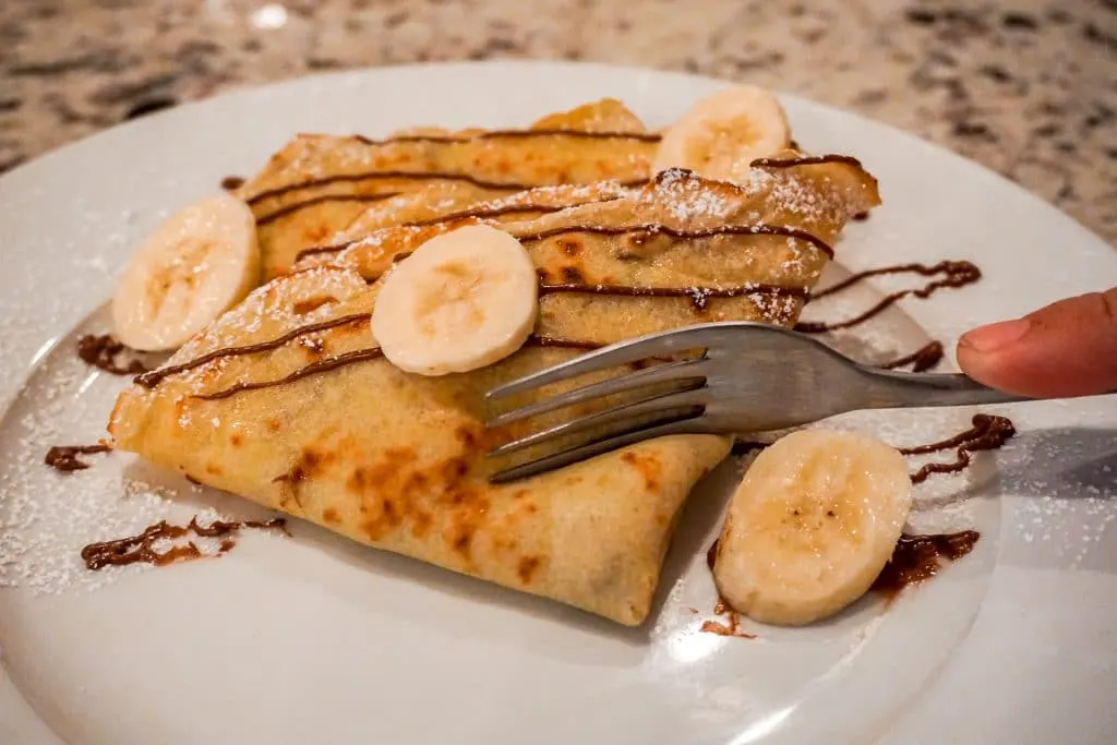 Someone using a fork to cut into a sweet crepe filled with fresh bananas and Nutella.