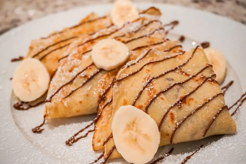 A side photo of three triangular sweet crepes stacked on top of each other filled with fresh bananas and Nutella. 