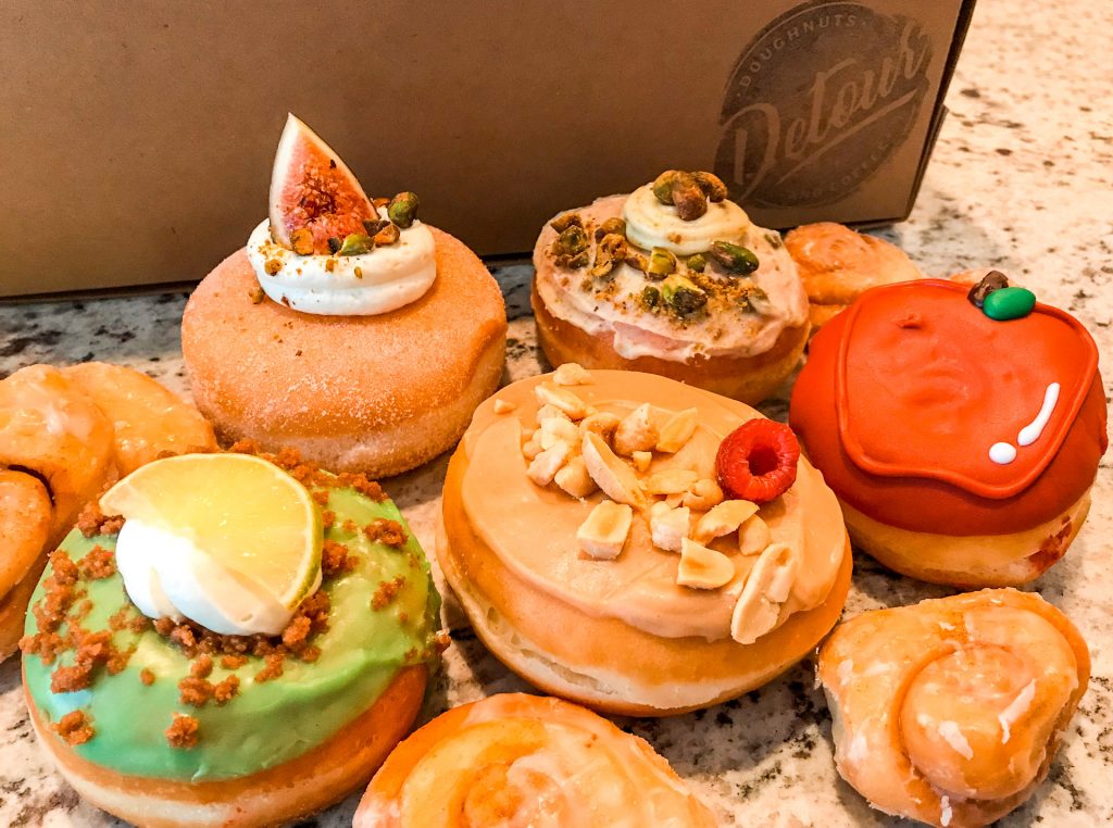 An array of gourmet donuts from Detour Donuts. Pictured is a green Key Lime donut, a red apple donut, a donut with peanuts, and more.
