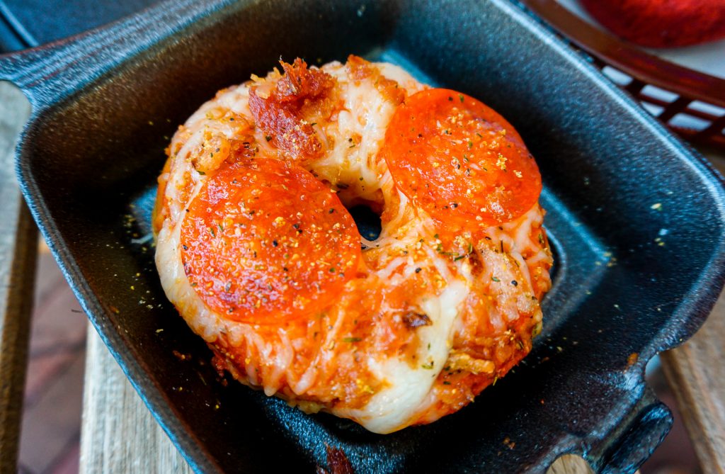A pizza donut from Urban Donut. It is a donut topped with cheese, pepperoni, bacon, and tomato sauce.