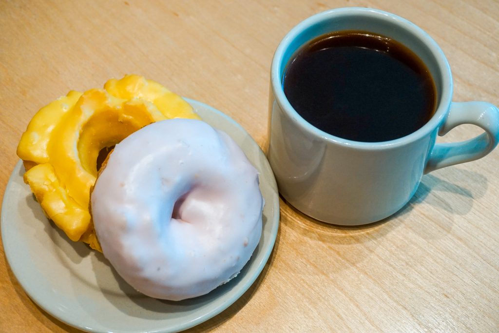 A blueberry cake donut stacked on top of a lemon ol-fashioned donut with a cup of black coffee from Top Pot Doughnuts.