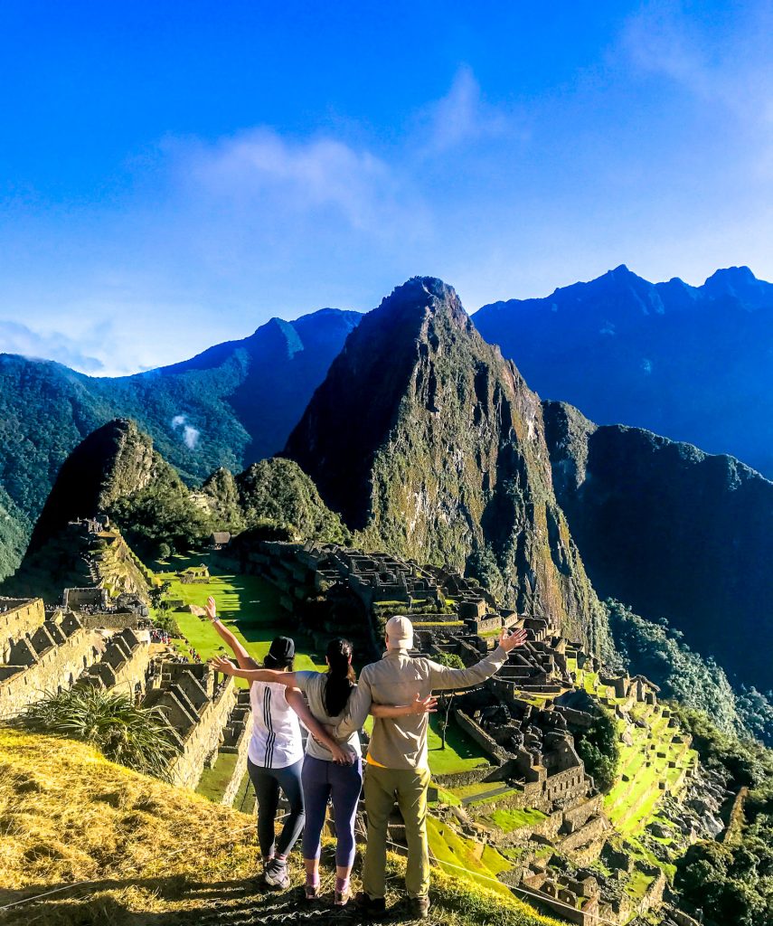 Three people standing with their arms out looking towards Machu Picchu - one of the greatest destinations in the world. 