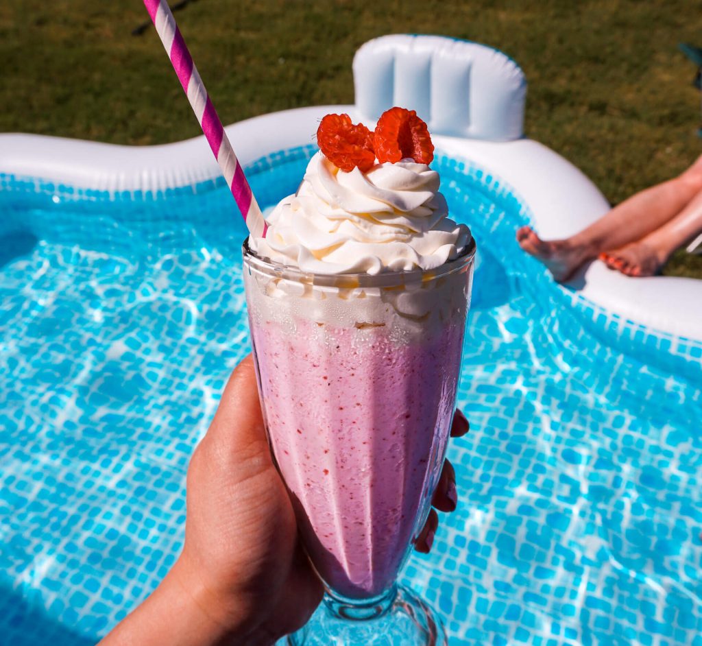 Someone holding a Pink Sand Beach cocktail above an inflatable pool filled with water.