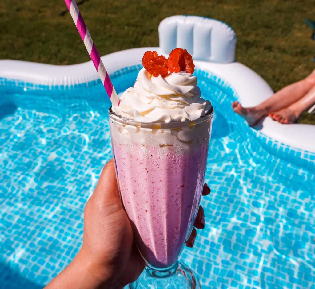 Someone holding a Pink Sand Beach cocktail above an inflatable pool filled with water.