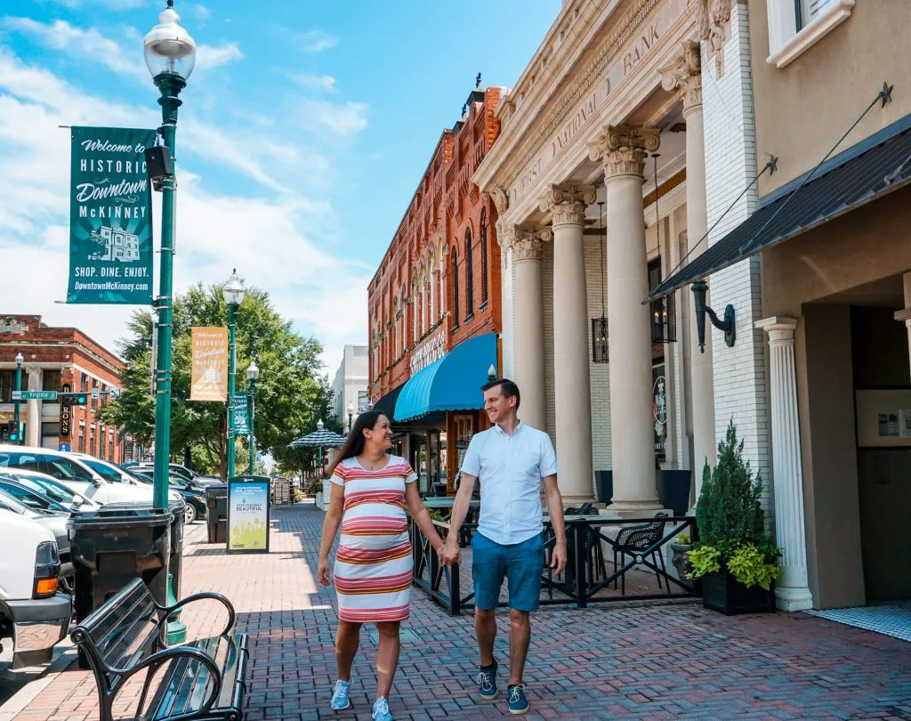 An expecting couple walking in historic downtown McKinney, Texas, one of the best babymoon destinations around the world. 