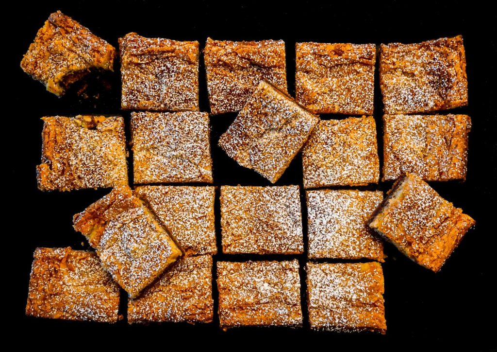 A bird-eye view of Chocolate Peanut Butter Gooey Butter Cake cut in squares displayed in a rectangle and on top of each other. 