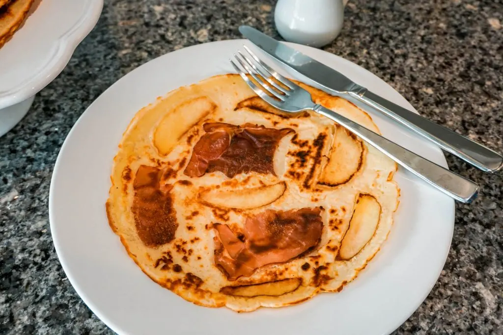 A Dutch pancake (pannekoek) with prosciutto (bacon) and apples on a plate with a fork and knife.
