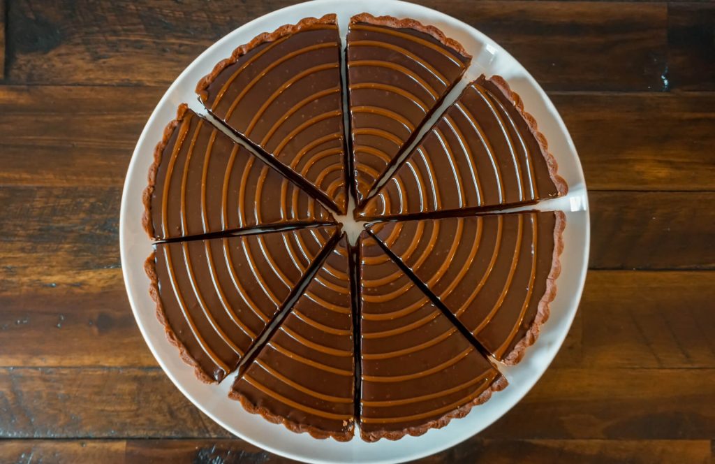 Birdseye view of a whole chocolate caramel tart sliced individually with caramel drizzled on top.