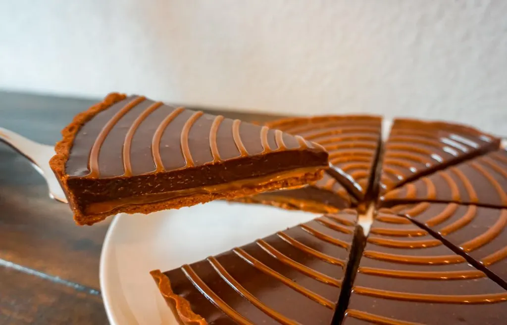 A beautiful slice of chocolate caramel tart being lifted with a pie server. 