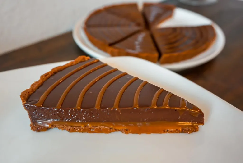 A chocolate caramel tart slice showing a creamy caramel layer on the bottom and a silky smooth chocolate ganache layer on top.