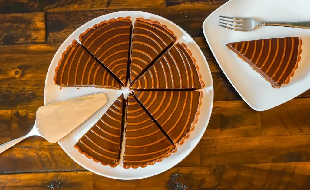 A pie server on a plate with several chocolate caramel tart slices on one plate and a small plate with one slice on the right.