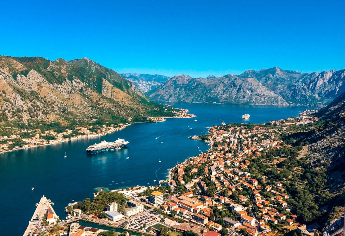 Scenic view of rolling mountains towering over Bay of Kotor's deep blue waters and red roof houses.