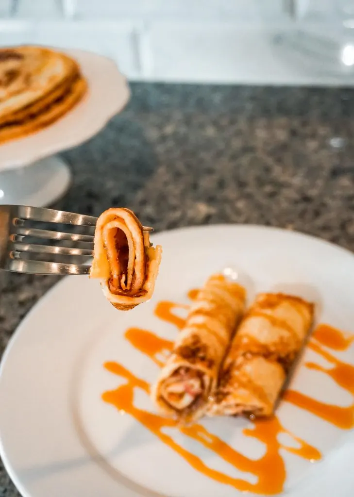 A Dutch pancake rolled up on a fork and on a plate with apple Stroop drizzled on top.