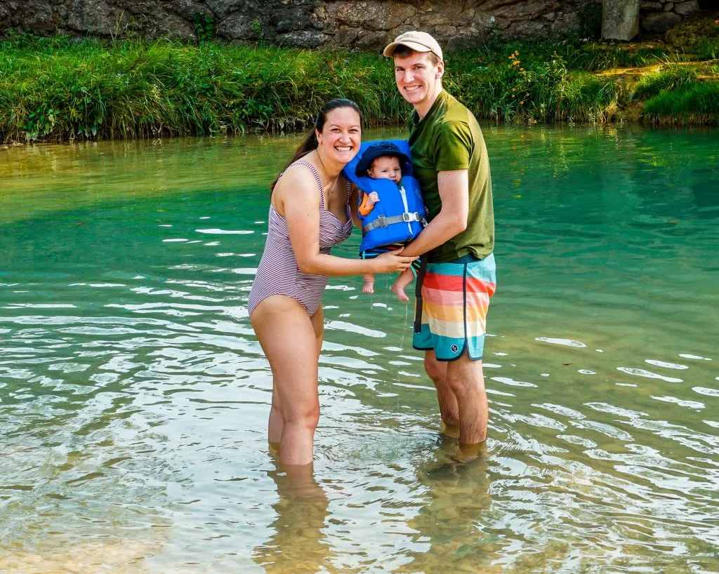Family holding their baby boy in a life jacket in a swimming hole at Turner Falls Park. 