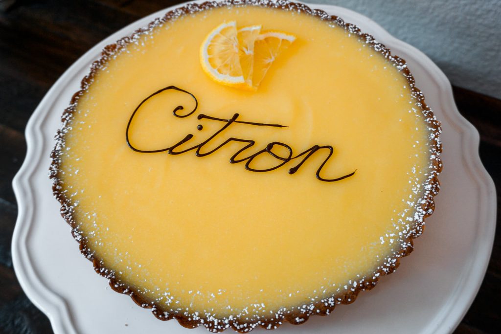 A classic French Lemon Tart (Tarte au Citron) with "Citron" written in cursive out of chocolate.