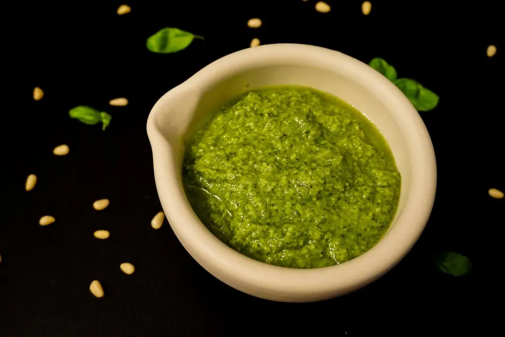 A mortar of homemade pesto with pine nuts and basil leaves around it.
