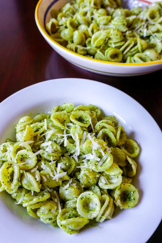 A close up on a plate of pesto orecchiette with a big bowl of it in the background.