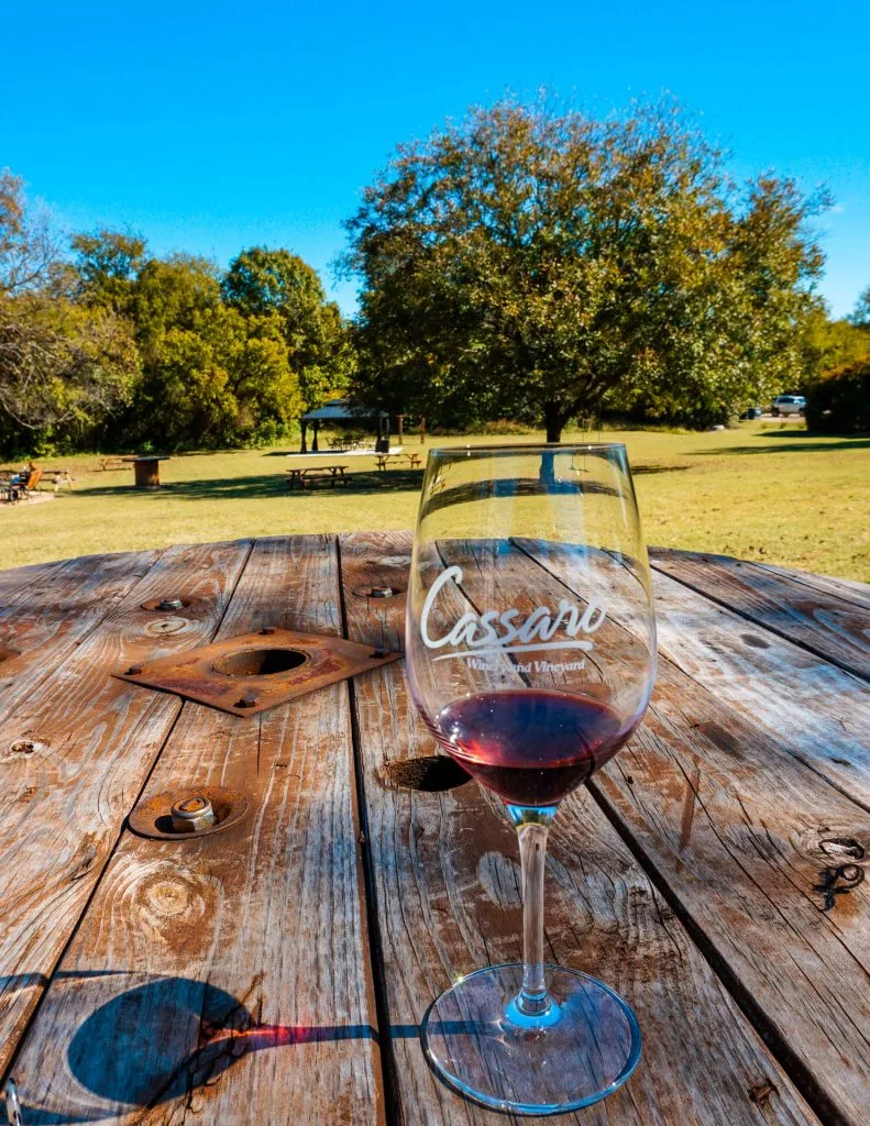 A glass of red wine on a wooden table from one of the best wineries in North Texas, Cassaro Winery and Vineyard.
