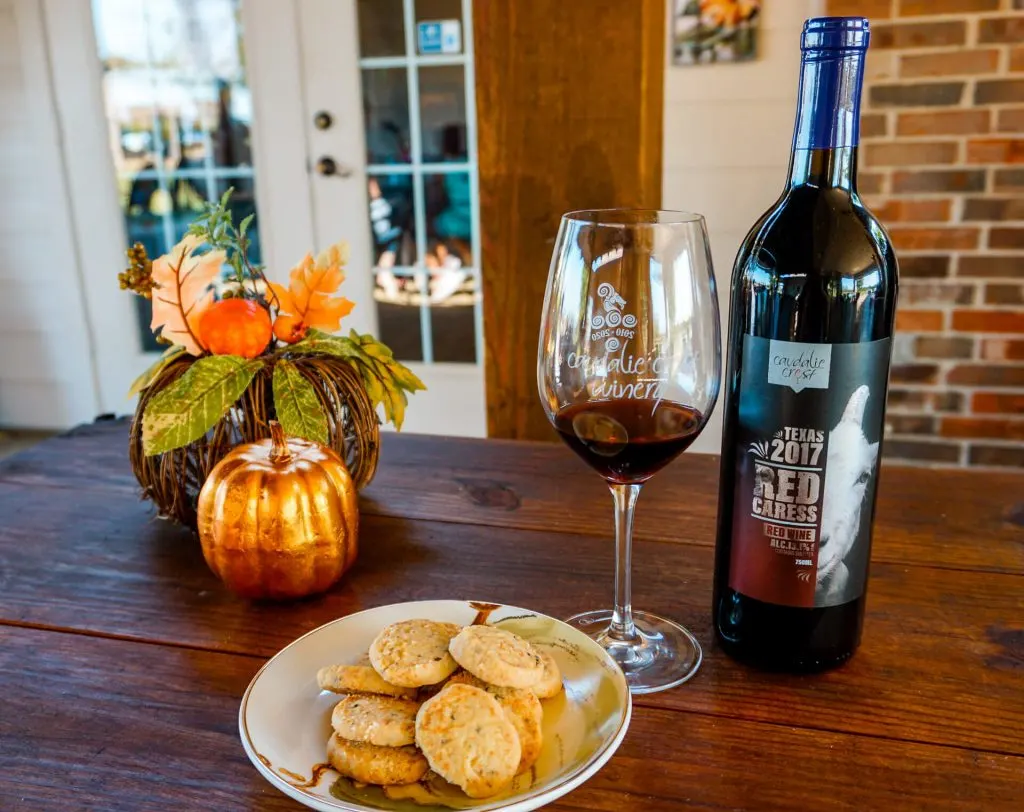 Decorative pumpkins, a plate of Sue's savory shortbread cookies, a glass of red wine, and a bottle of wine from Caudalie Crest Winery & Vineyard in Celina, Texas.