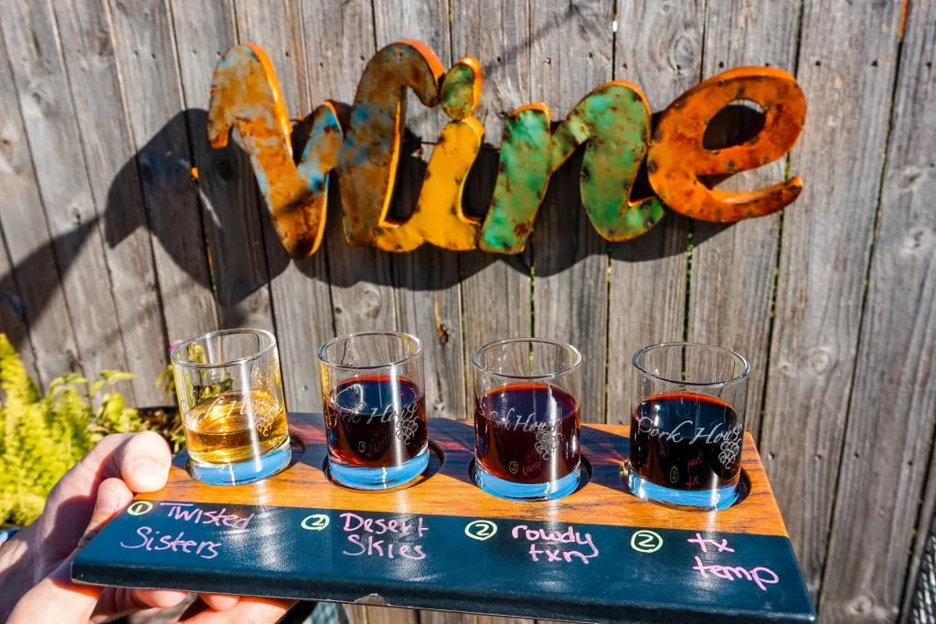 A wine flight from Cork House in front of a Wine sign on a wooden fence.