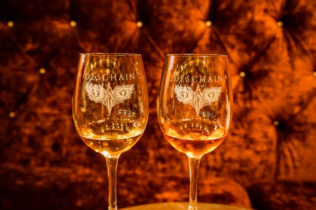 Two glasses from Deschain Cellars with a velvet couch in the background.