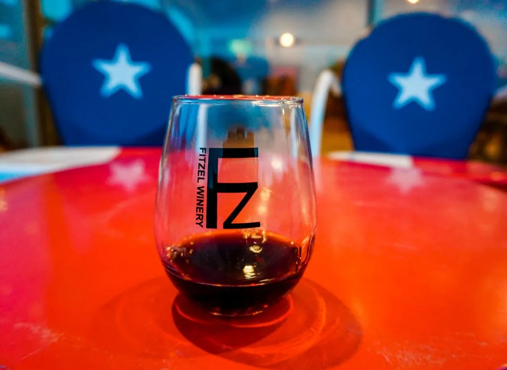 A glass of red wine in a stemless glass from Fitzel Winery with two chairs in the background with the Texas star.