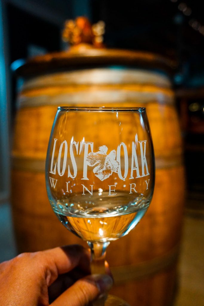 A glass of white wine from Lost Oak Winery in front of a wooden barrel. 