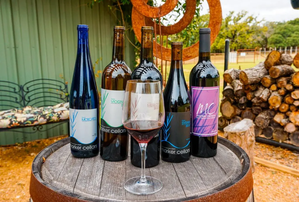 A glass of red wine in front of several bottles of wine from Marker Cellars.
