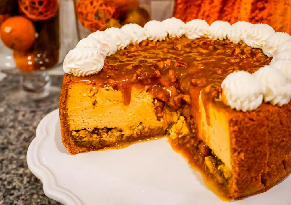 A 9 inch Pumpkin Pecan Cheesecake missing a giant slice with pecan caramel oozing down the sides.