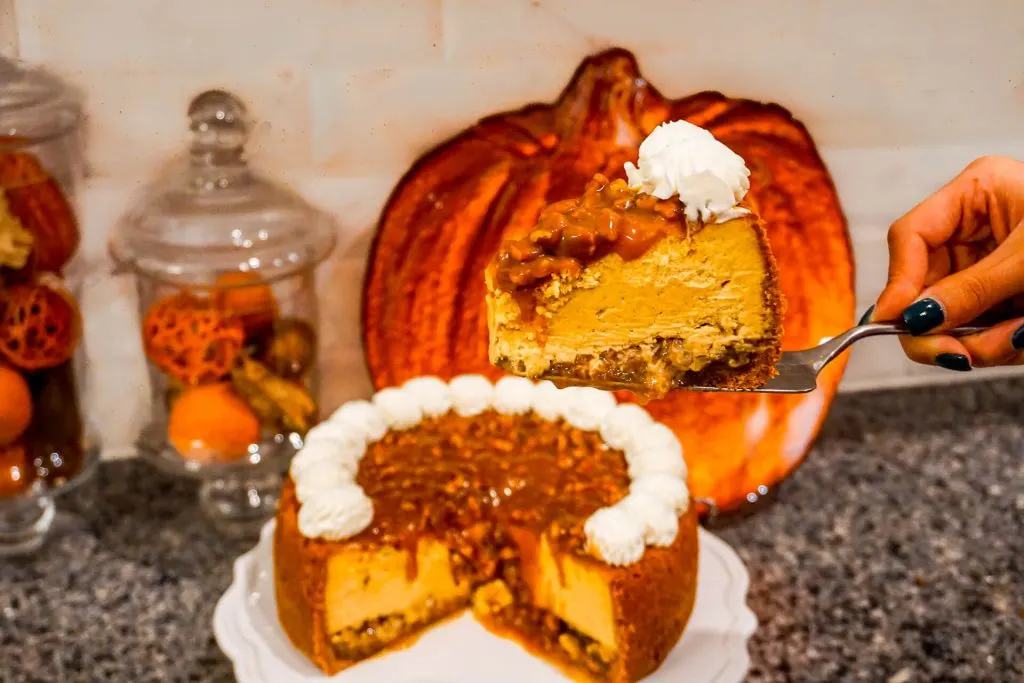 A slice of Pumpkin Pecan Cheesecake in focus with the whole cake in the background.