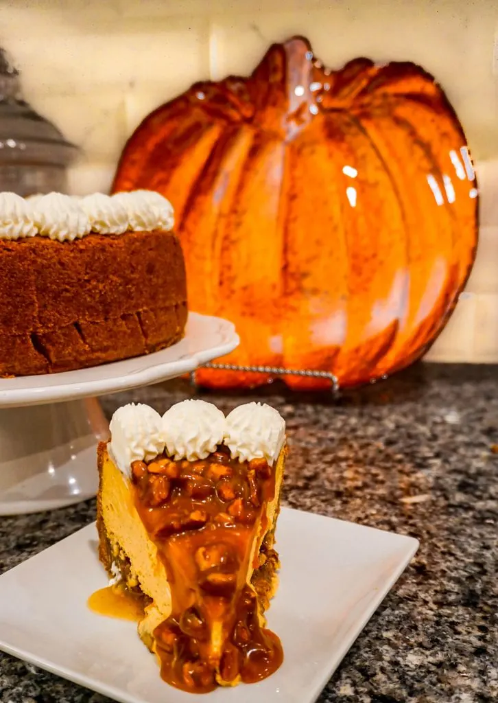 A slice of Pumpkin Pecan Cheesecake with pecan caramel oozing down the sides.