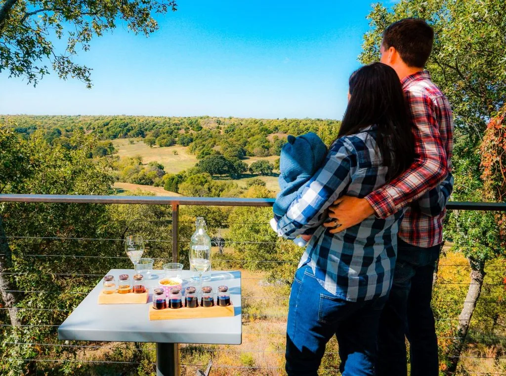 A couple with a baby looking out into the valley with a wine tasting at one of the best wineries in North Texas, 4R ranch Vineyards & Winery.