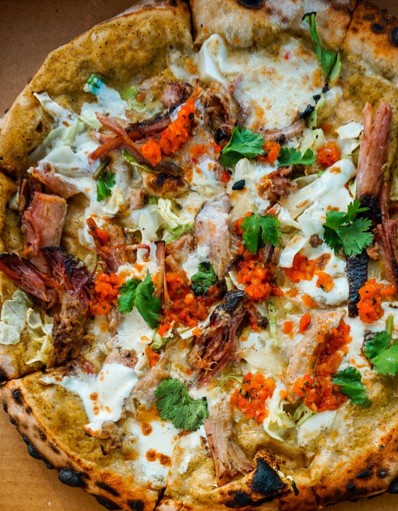 A birdseye view of pizza topped with braised pork, mozzarella, Fresno chili salsa, cilantro, and tomatoes from Jester King Brewery in Austin, Texas.