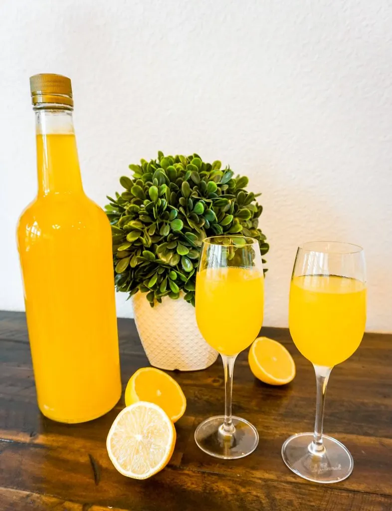 A bottle of homemade limoncello with two glasses full of limoncello and slices of lemons surrounding it.